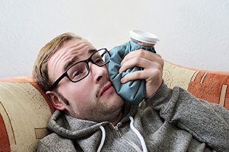 A guy laying with a cold compress on his cheek