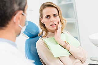 A woman in the dentist chair with her hand on her cheek